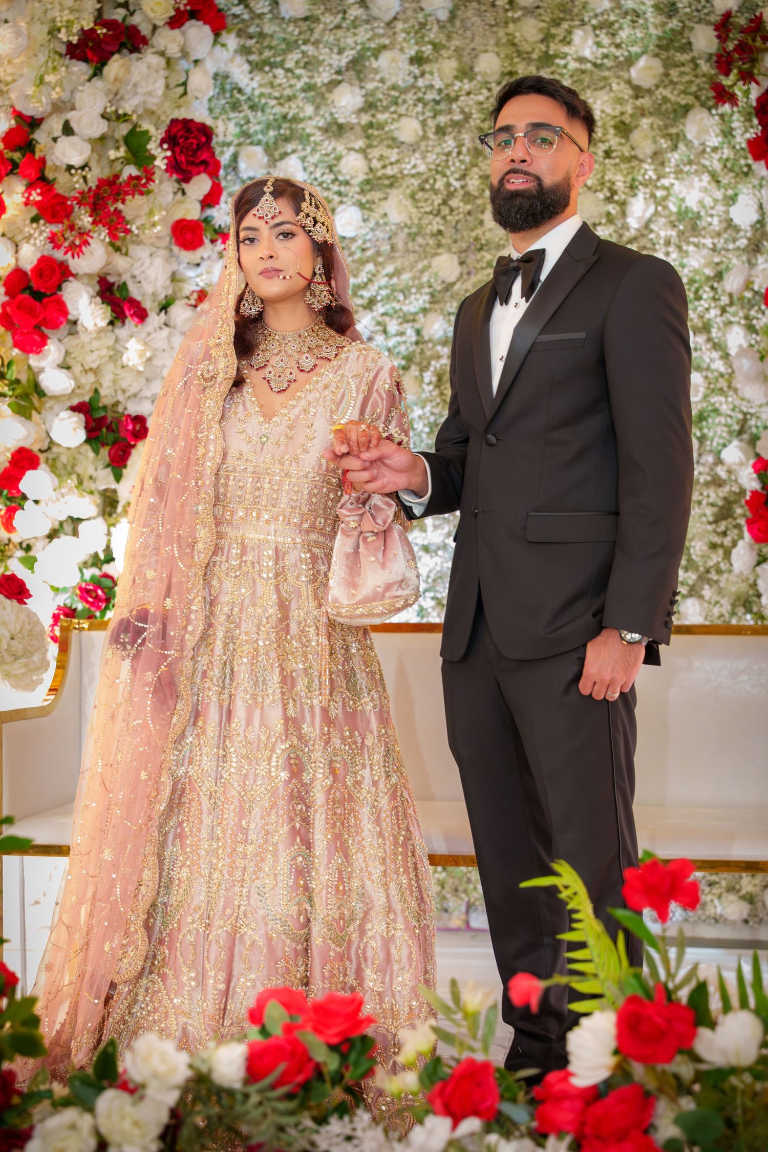Wedding couple posing against a floral wall with red and white roses.