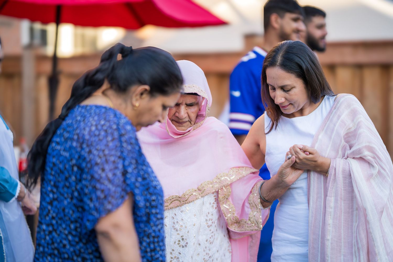 Three women in colorful attire laugh and share a joyful moment at an outdoor celebration.