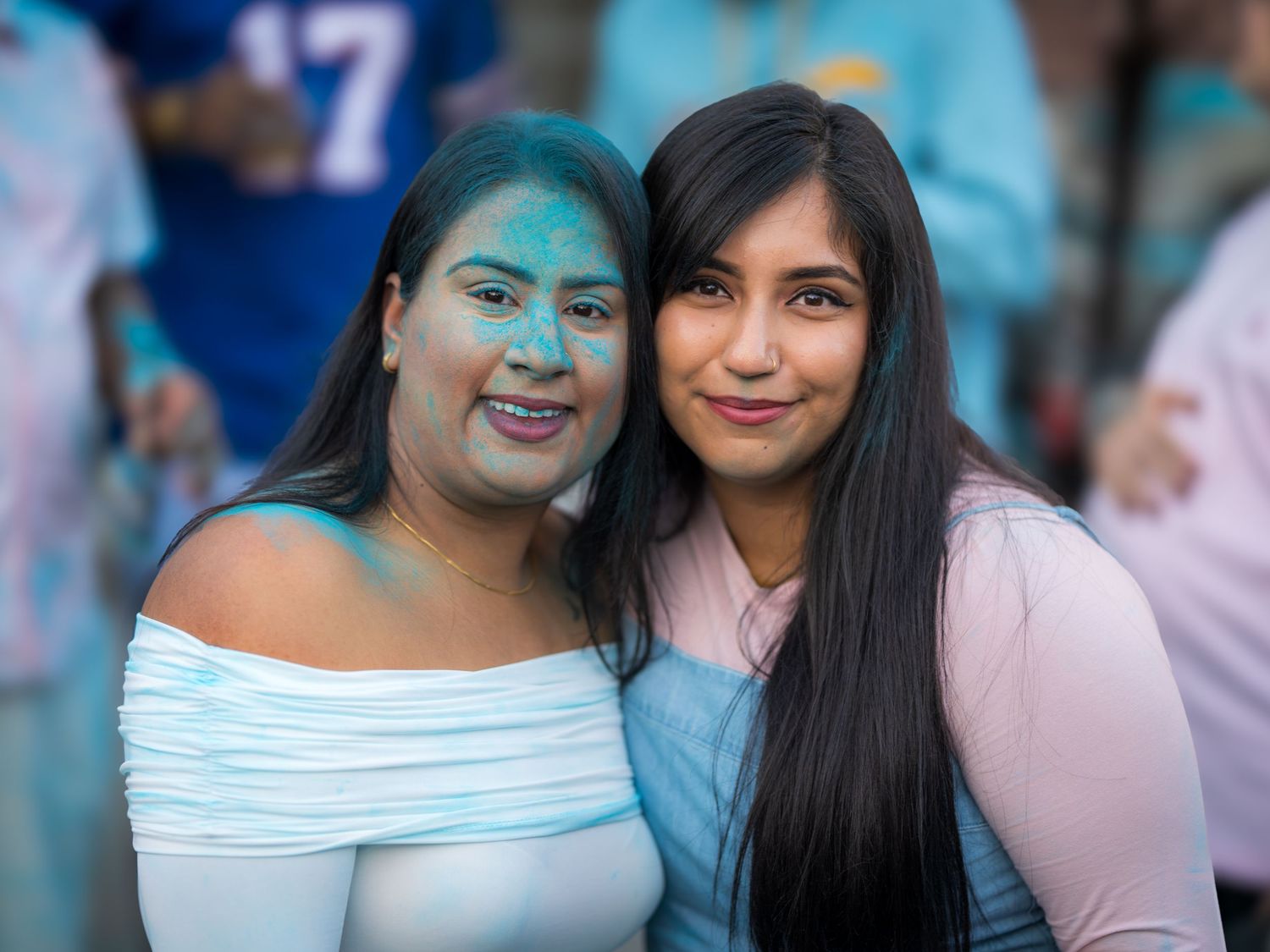 Two women smiling together covered in blue powder at a gender reveal party.