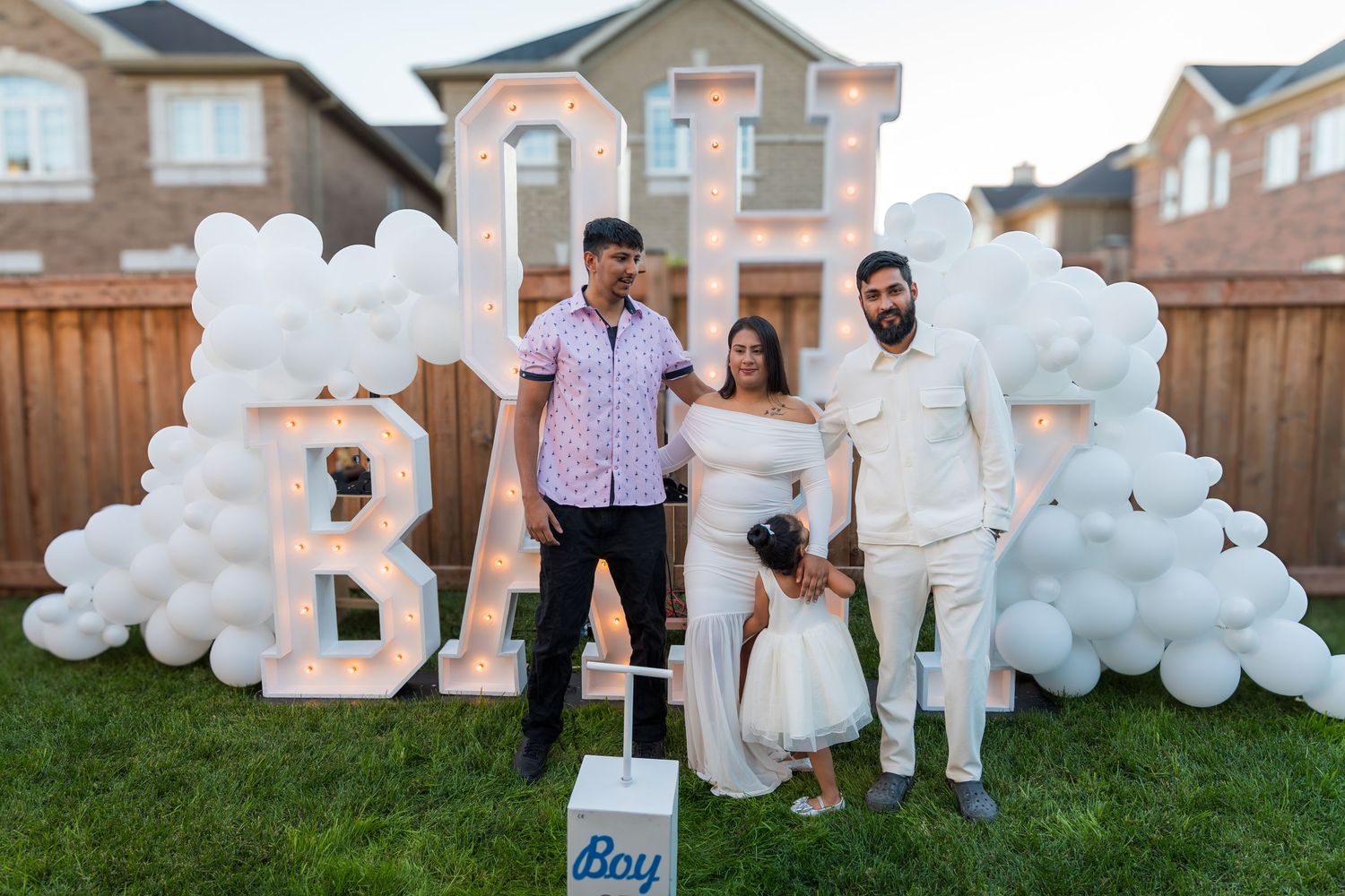 Couple with child at gender reveal party with OH BABY marquee letters and white balloons.