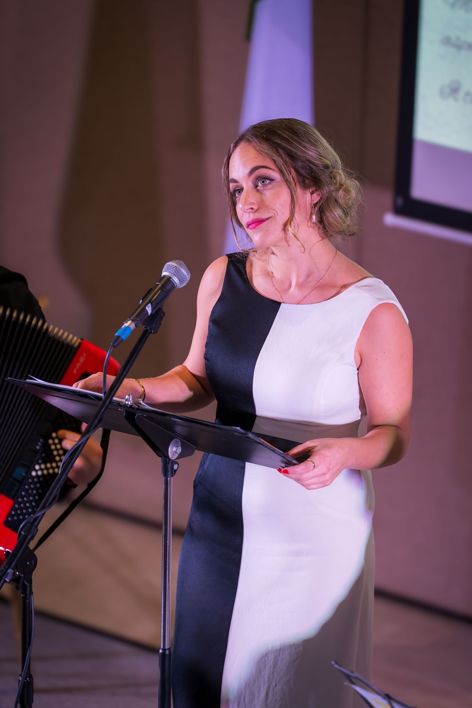 Elegant woman in black and white dress speaking at a podium microphone during a formal event.