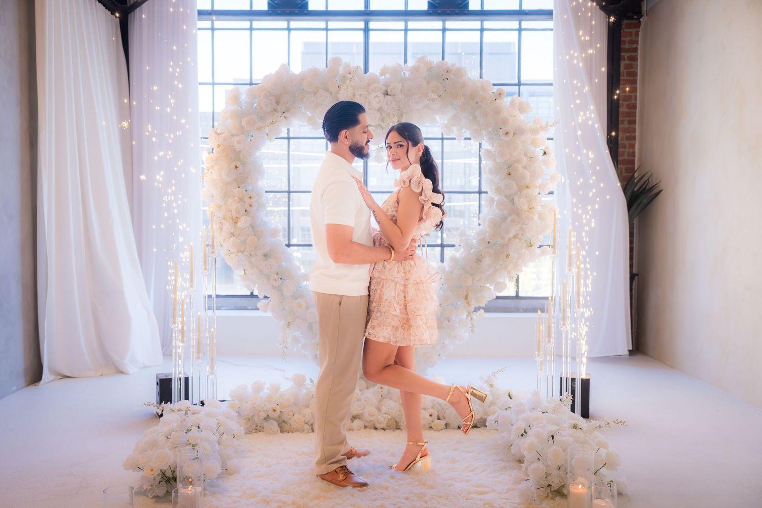 Man and woman sharing a tender moment under a heart-shaped floral arch with fairy lights.