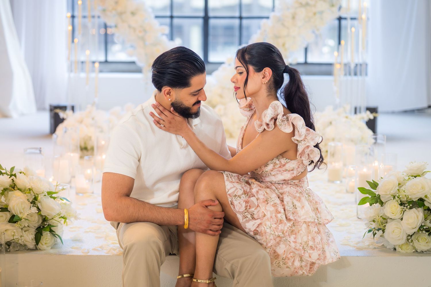 Loving couple sitting close together, sharing an intimate moment in elegantly decorated white venue.