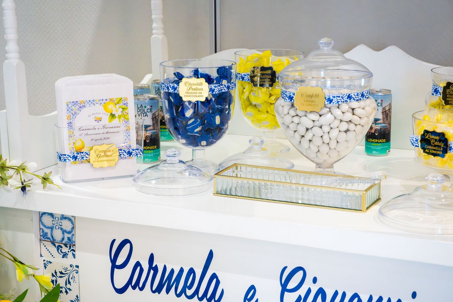Candy bar display labeled Carmela e Giovanni with blue and yellow themed sweets in glass jars.