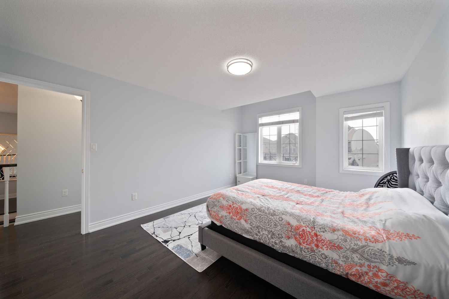 Modern bedroom interior with white walls, gray bedding, and coral accent pillows illuminated by recessed lighting.