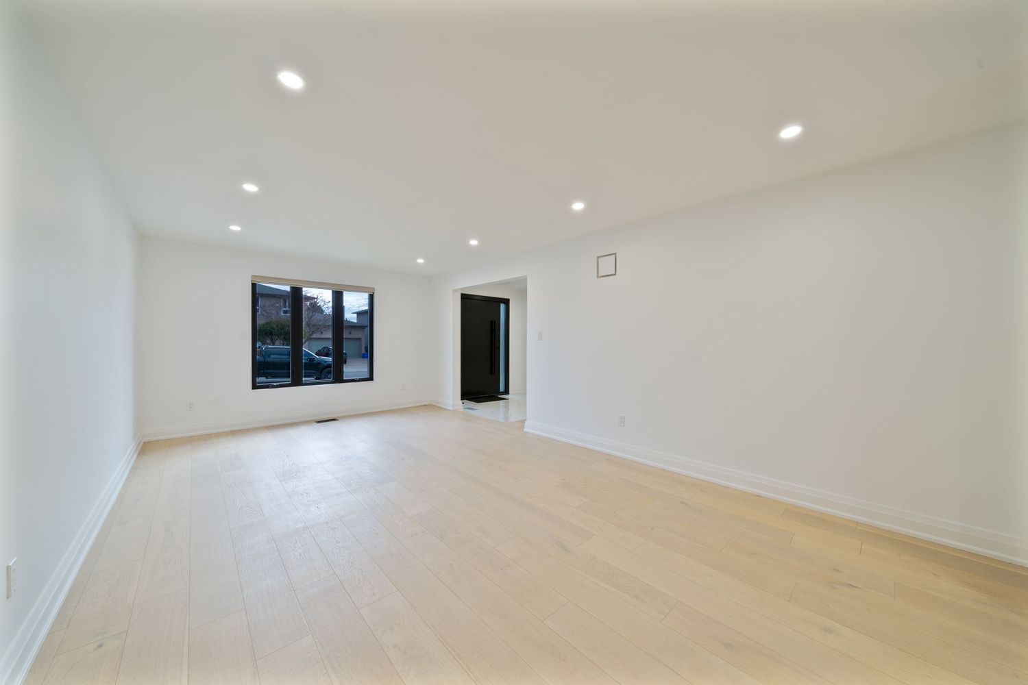 Modern white hallway with recessed lighting and light hardwood flooring extends into bright open space.