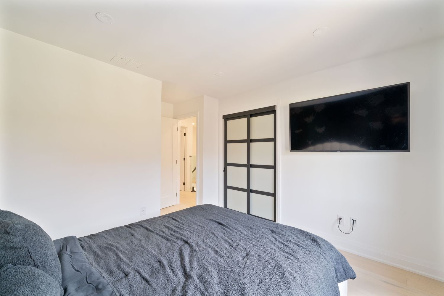Modern bedroom interior with gray bedding, white walls, and natural light coming through windows.
