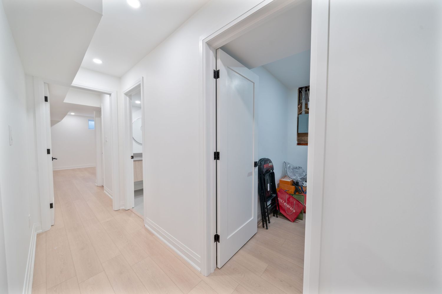 Modern basement hallway with white walls, recessed lighting, and beige carpeting leading to storage areas.