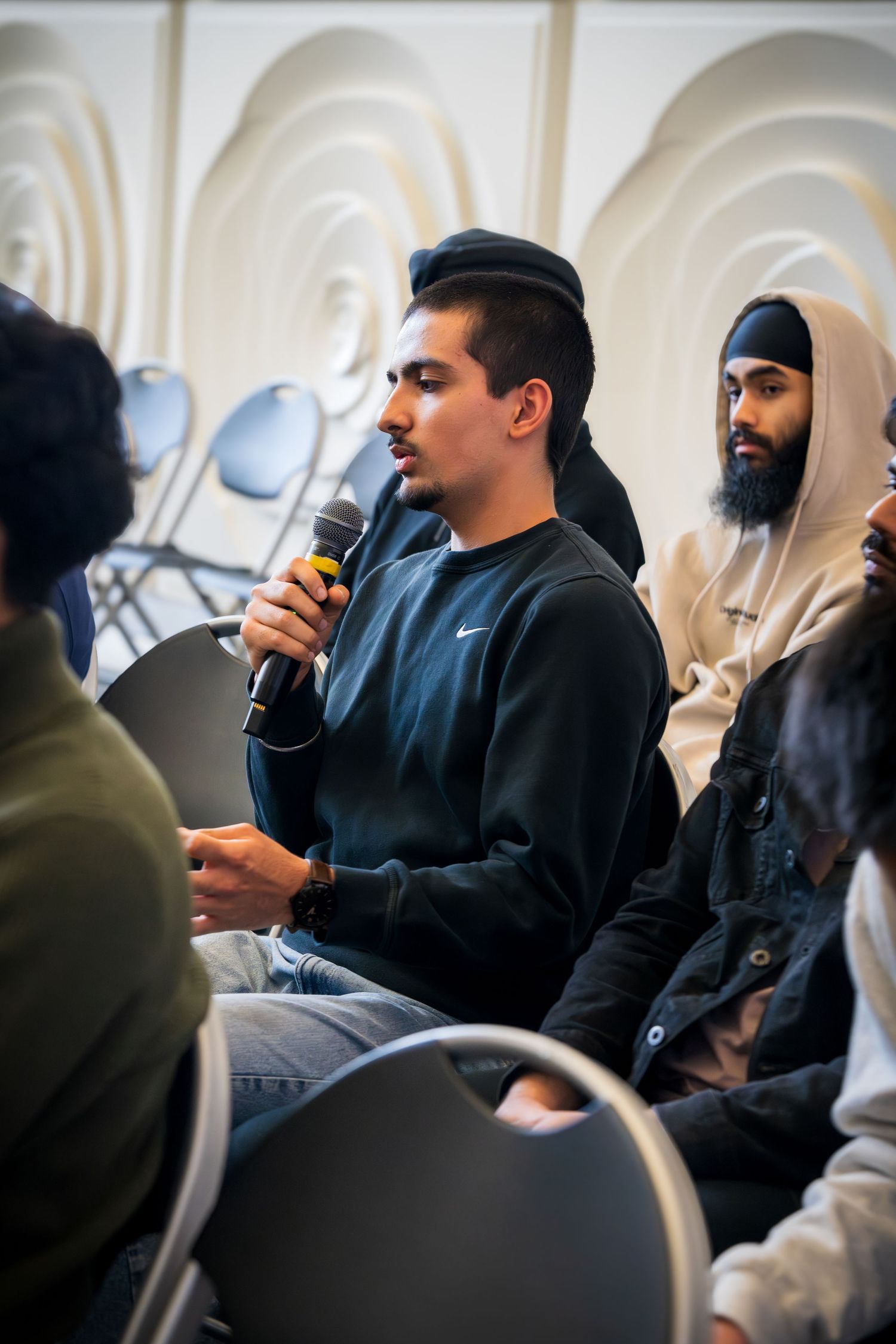 Panel discussion participants sit in chairs against a white textured wall during a professional event.