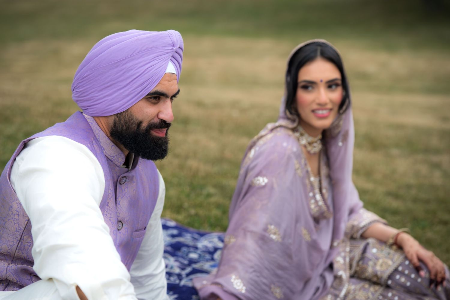 Couple in coordinating purple and white traditional outfits sitting together outdoors.