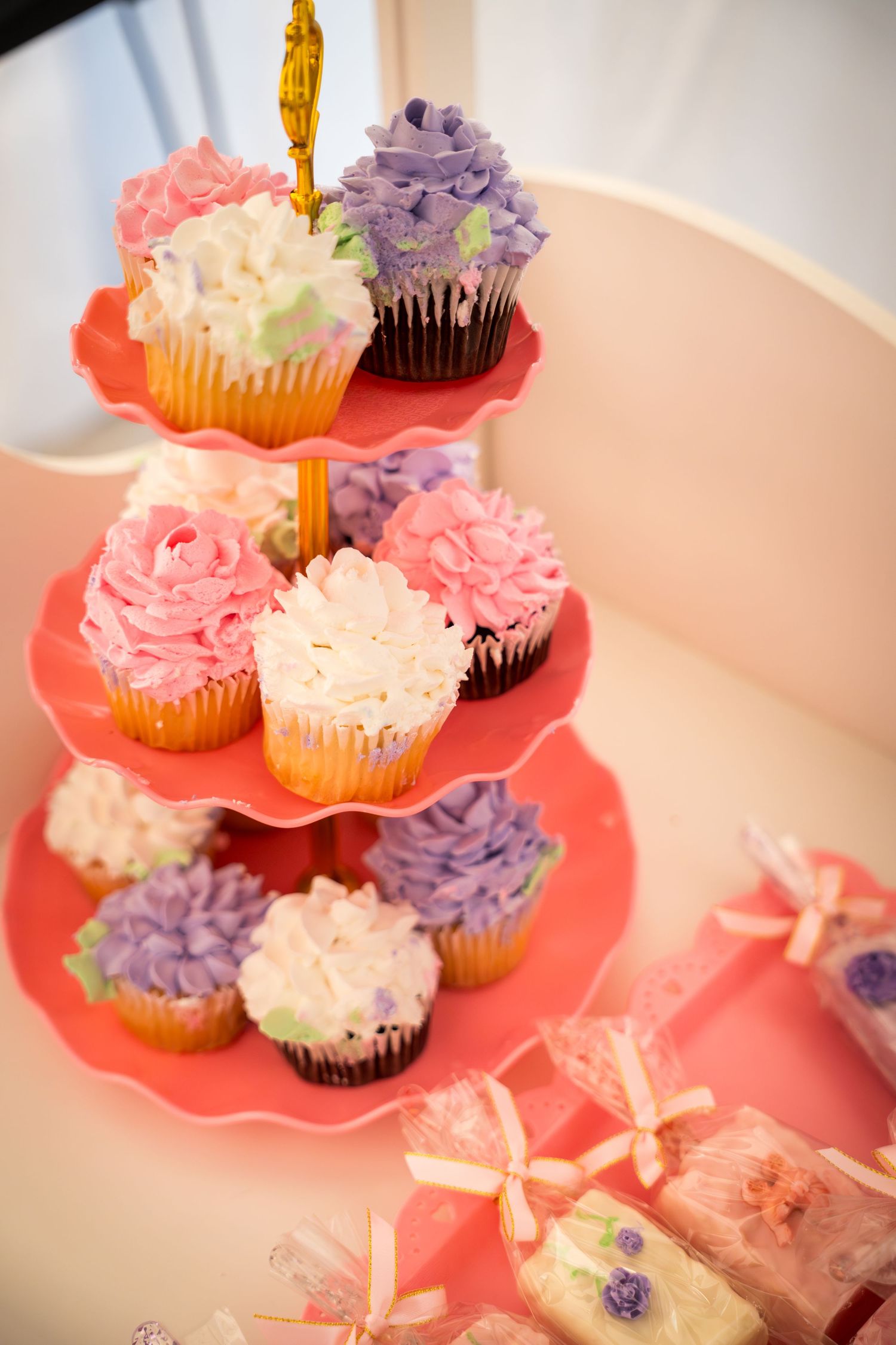 Tiered display of pink, purple and white frosted cupcakes on a coral-colored stand.