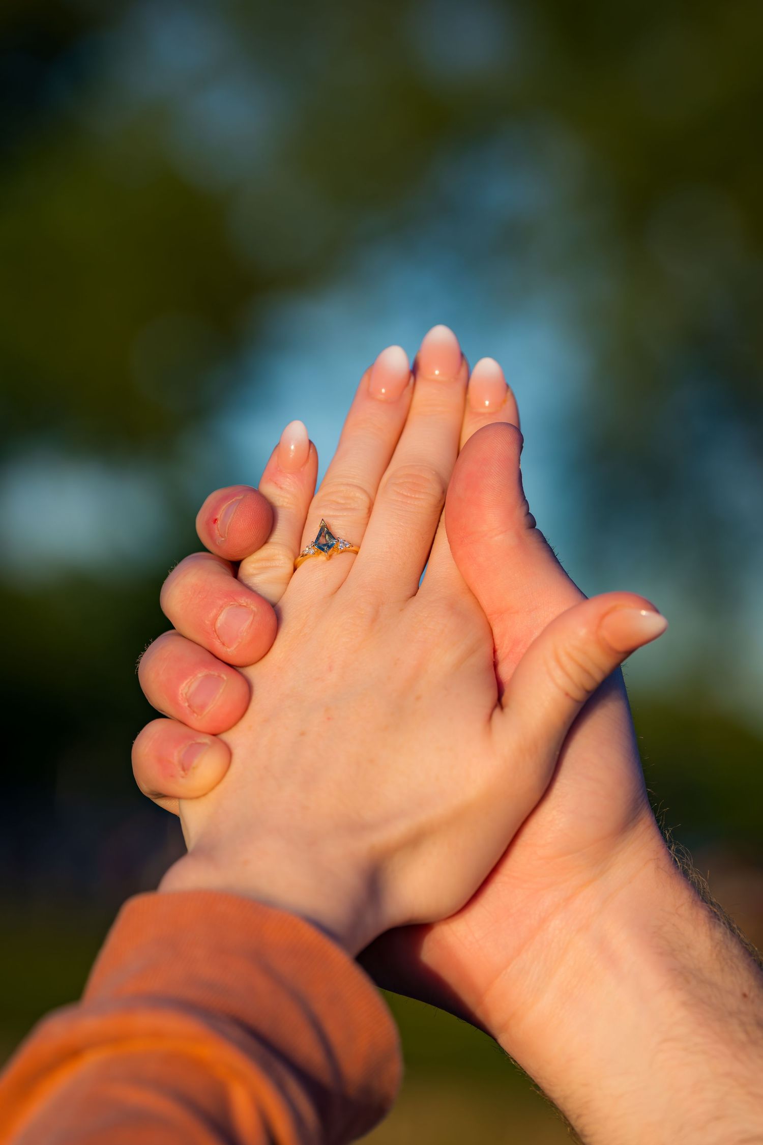 Close-up of a couple holding hands outdoors, woman wearing a diamond engagement ring.