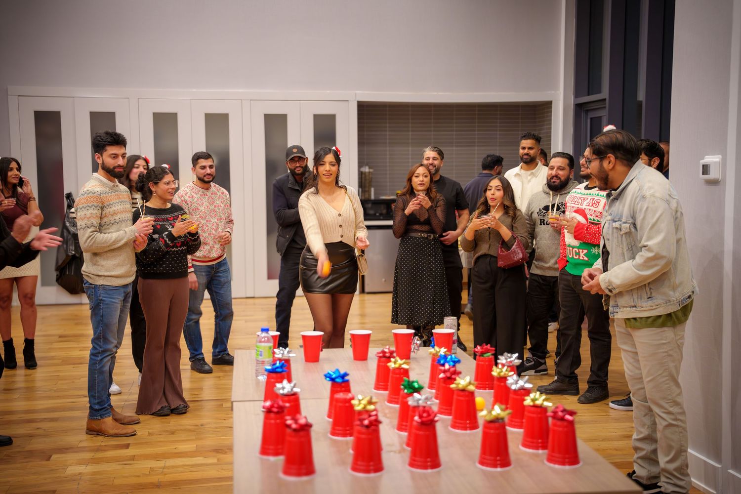 Red solo cups arranged in rows on a wooden floor with party guests gathered around.