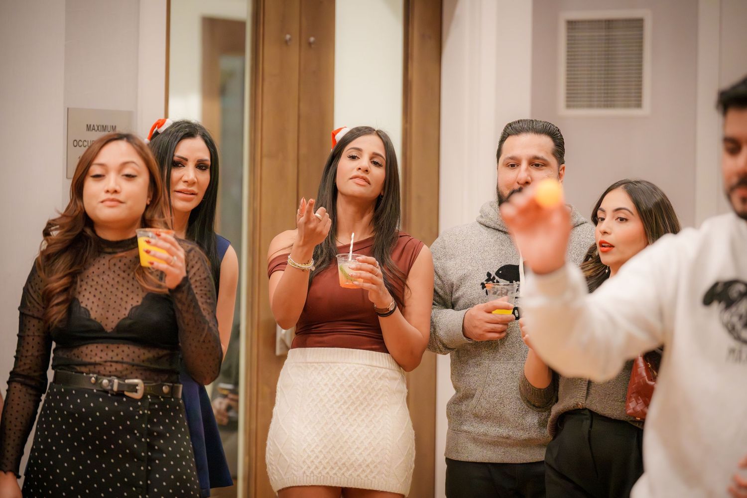 People mingling at an indoor social event with wooden doors visible in background.