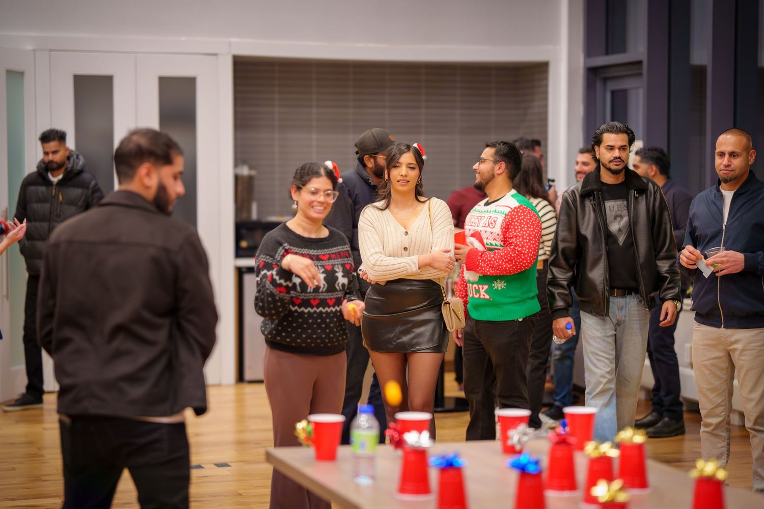 Wide view of an indoor holiday party with red cups and mingling guests.