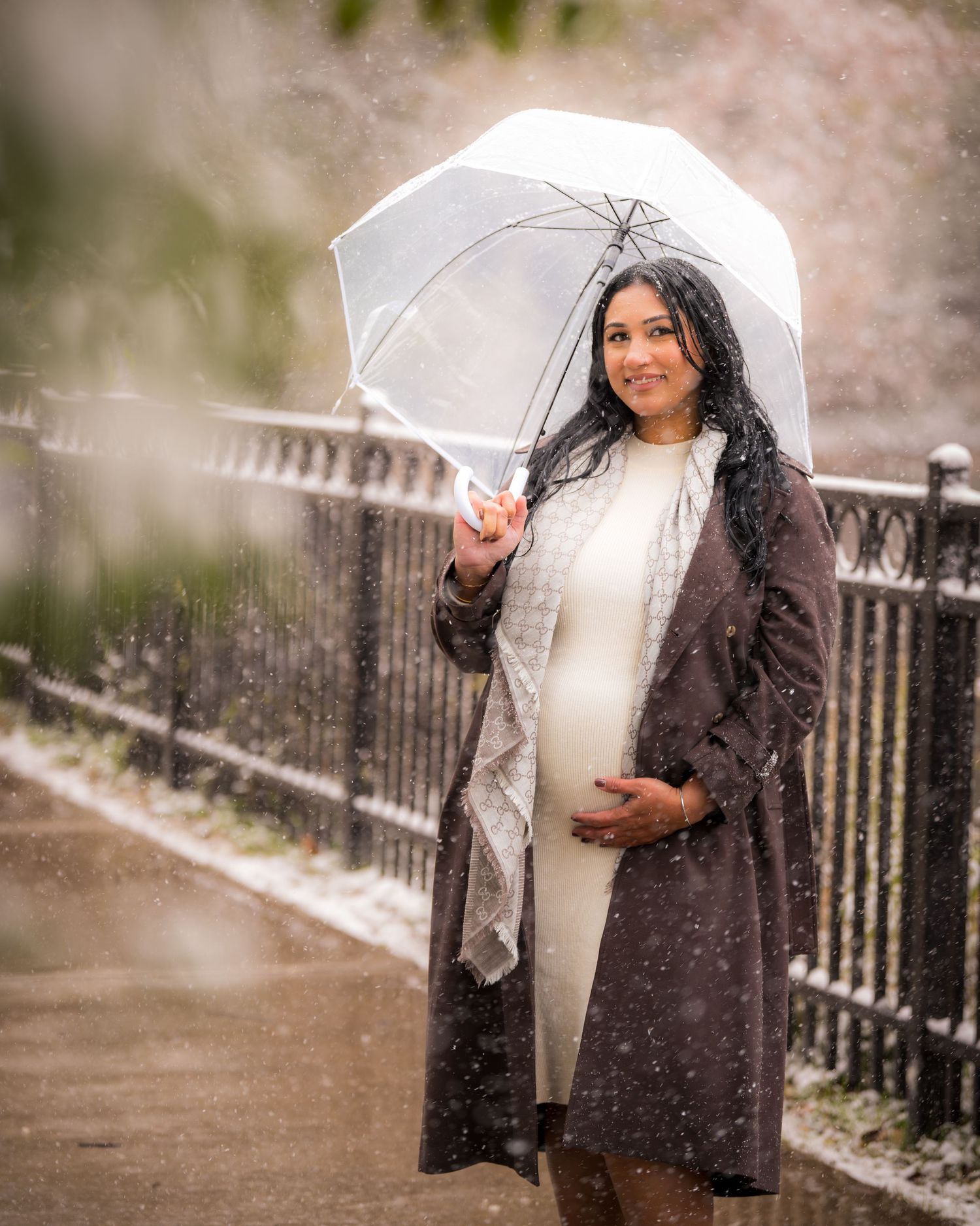 A couple stands under white umbrellas during a snowy engagement session.