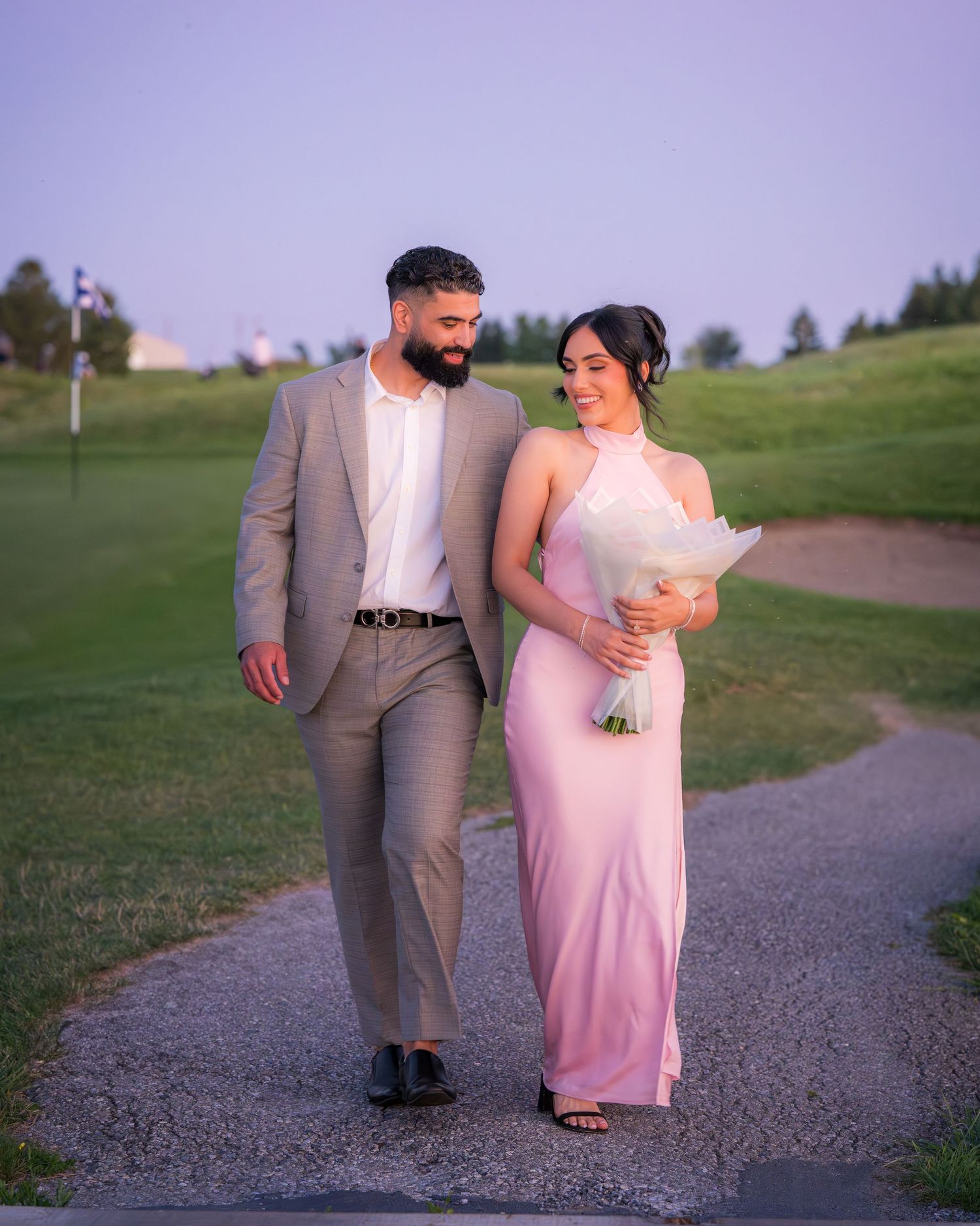 A couple walks together on a gravel path against a scenic outdoor background.