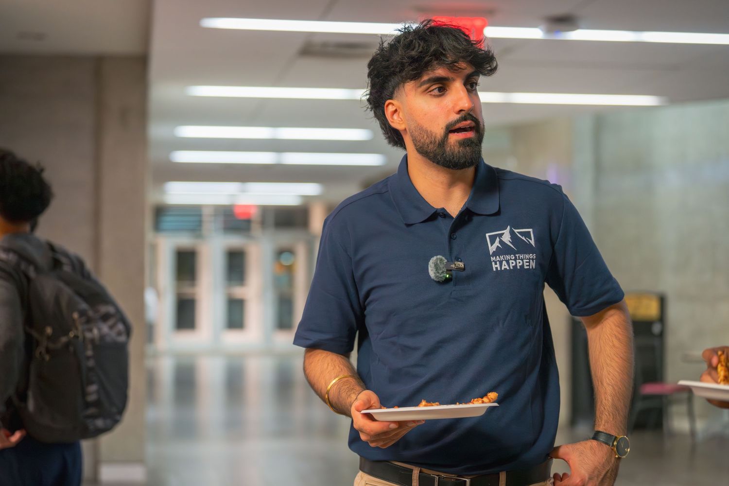 Staff member in navy branded polo carrying tablet in institutional hallway.