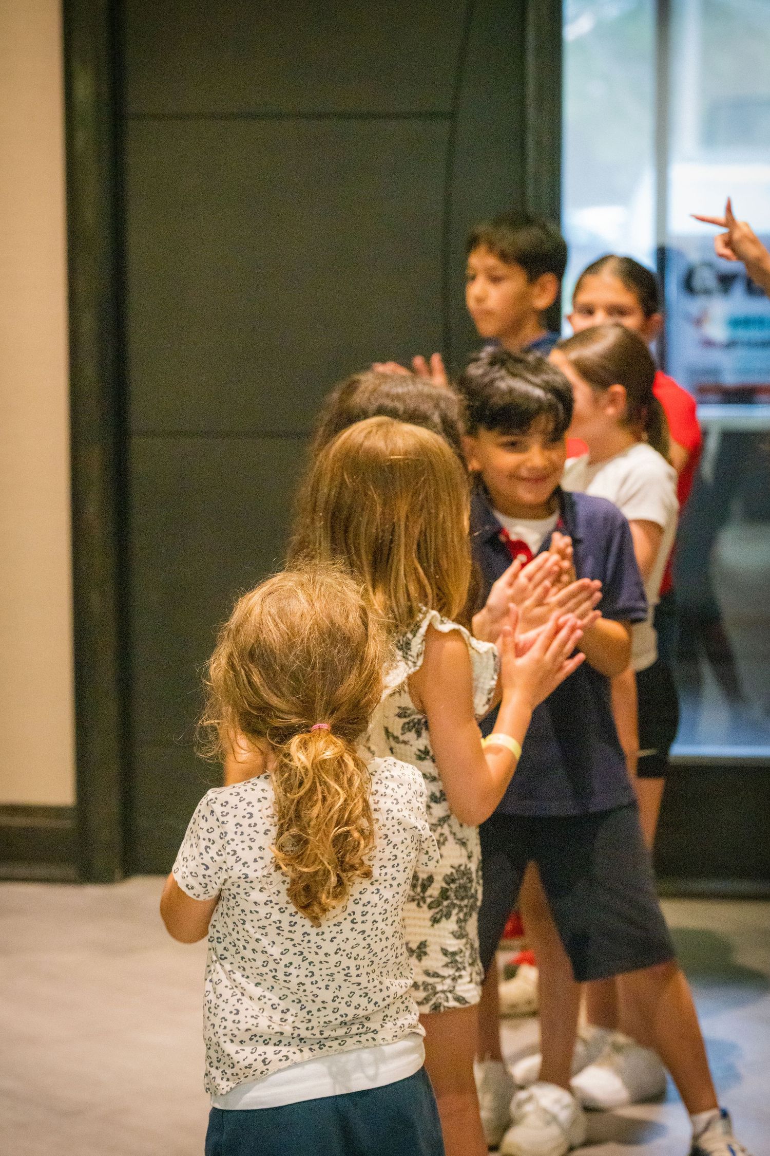 Group of children playing a clapping game together in a modern indoor space.
