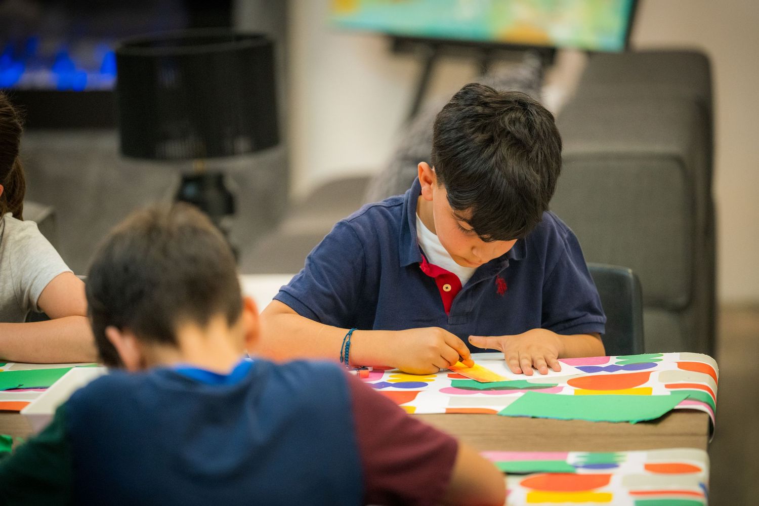 Young boy in navy polo shirt focused on cutting colorful paper during an art class activity.