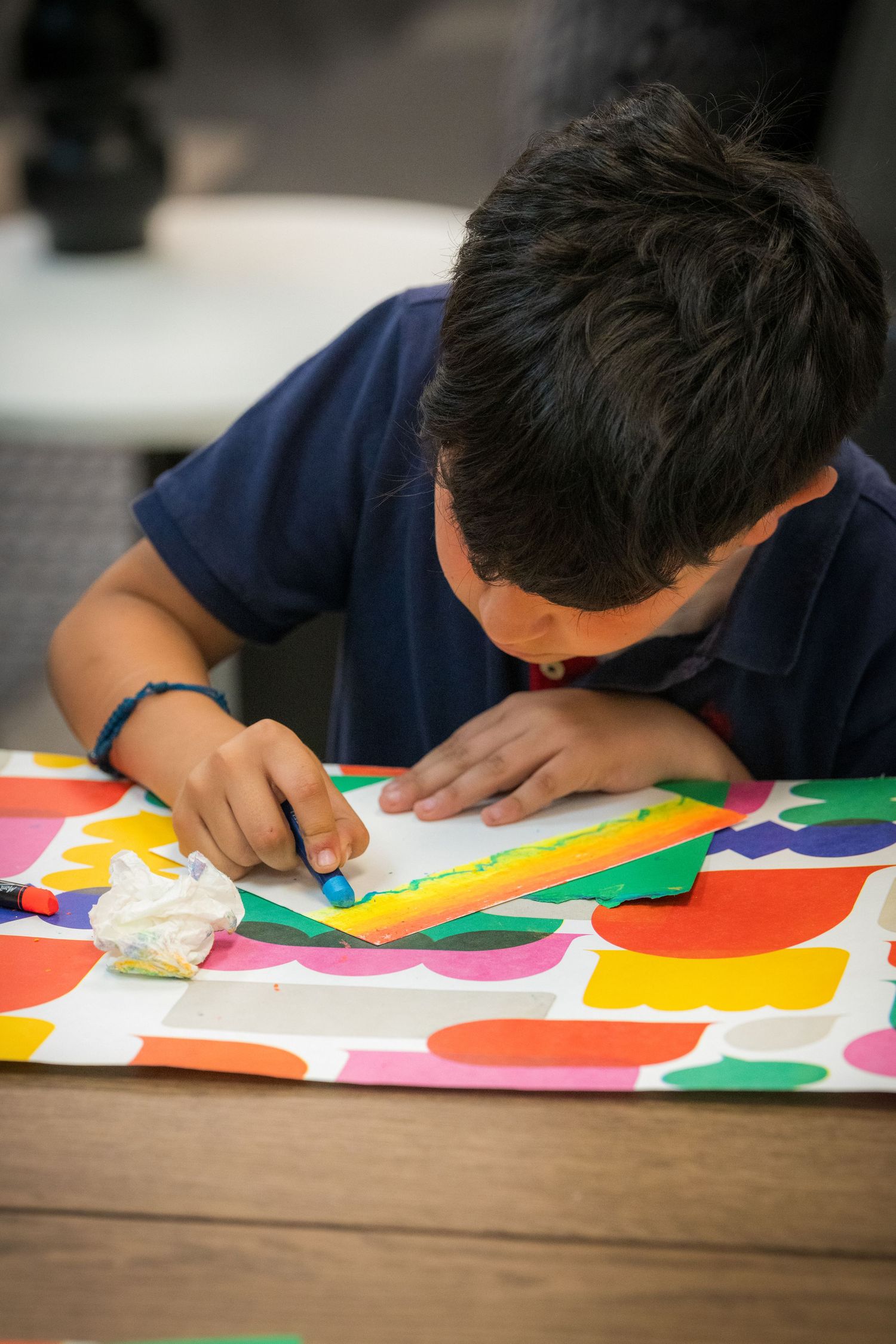 A focused boy uses crayons on a vibrant colorful paper art project at a table.