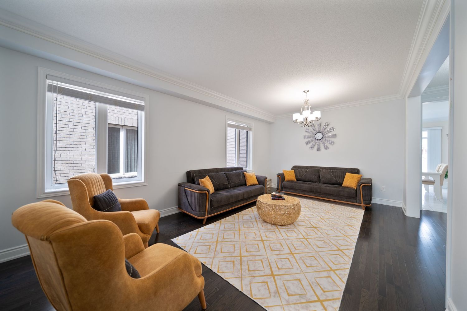 Modern living room with dark leather sofas, mustard accent chairs, geometric rug and starburst wall clock.