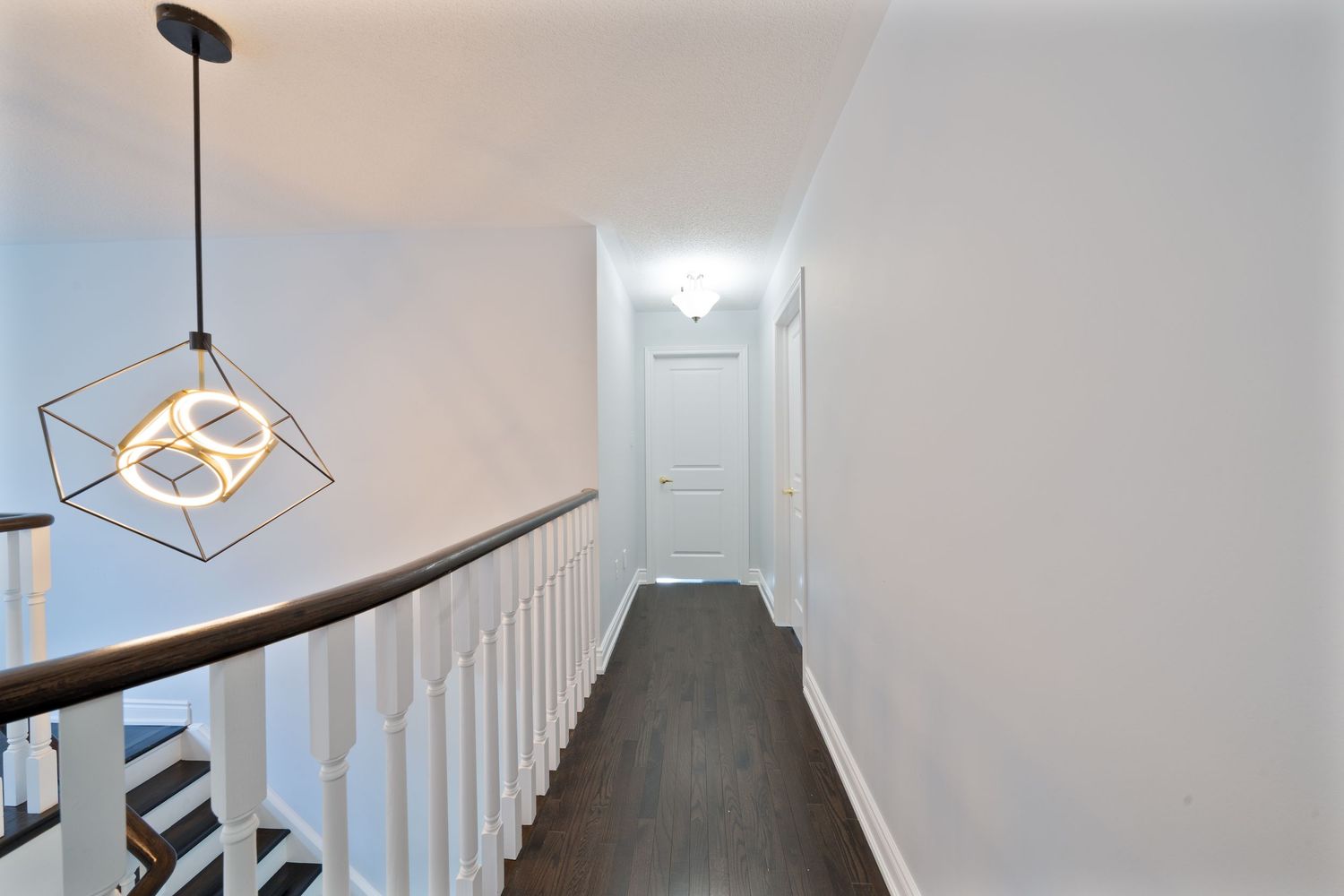 Modern pendant lights hang from a white ceiling in a contemporary hallway with geometric lighting fixtures.