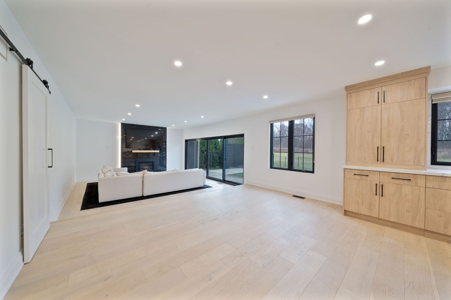 Modern open concept home interior with light wood floors, white walls, and recessed lighting throughout the space.