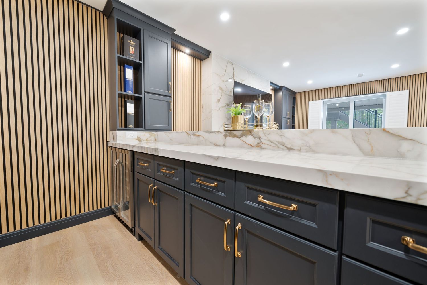 Modern kitchen design with vertical wood slats, white marble countertops, gold hardware and recessed lighting.