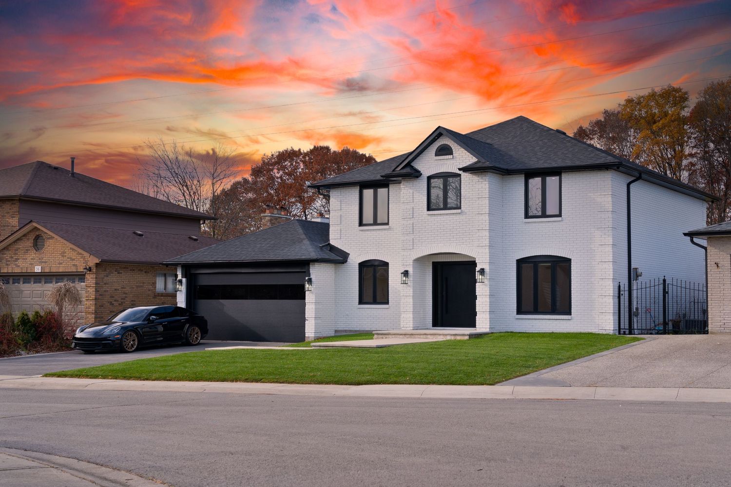 A row of modern suburban houses with white exteriors against a dramatic orange and pink sunset sky.