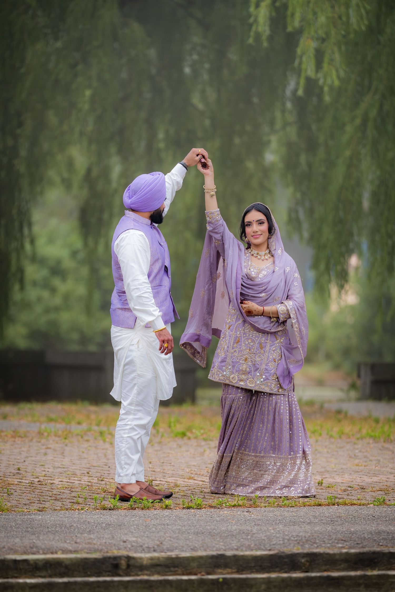 Traditional wedding photoshoot with couple in purple and white outfits posing under willow trees.
