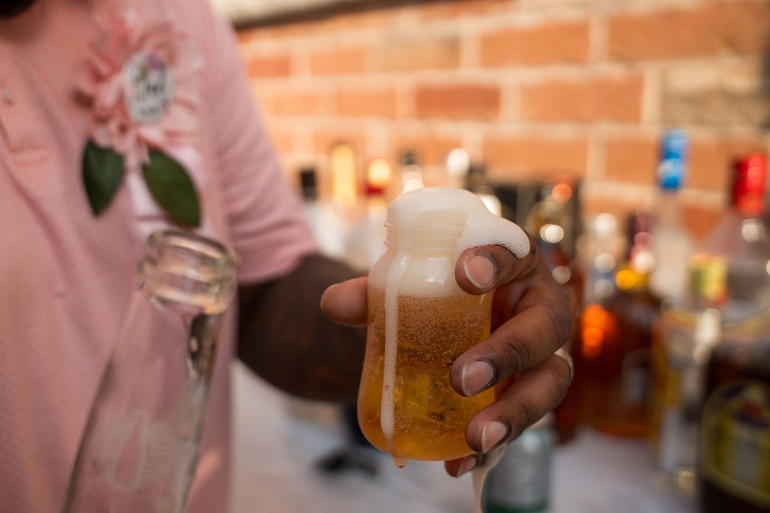 Person sipping beer against rustic brick wall backdrop.