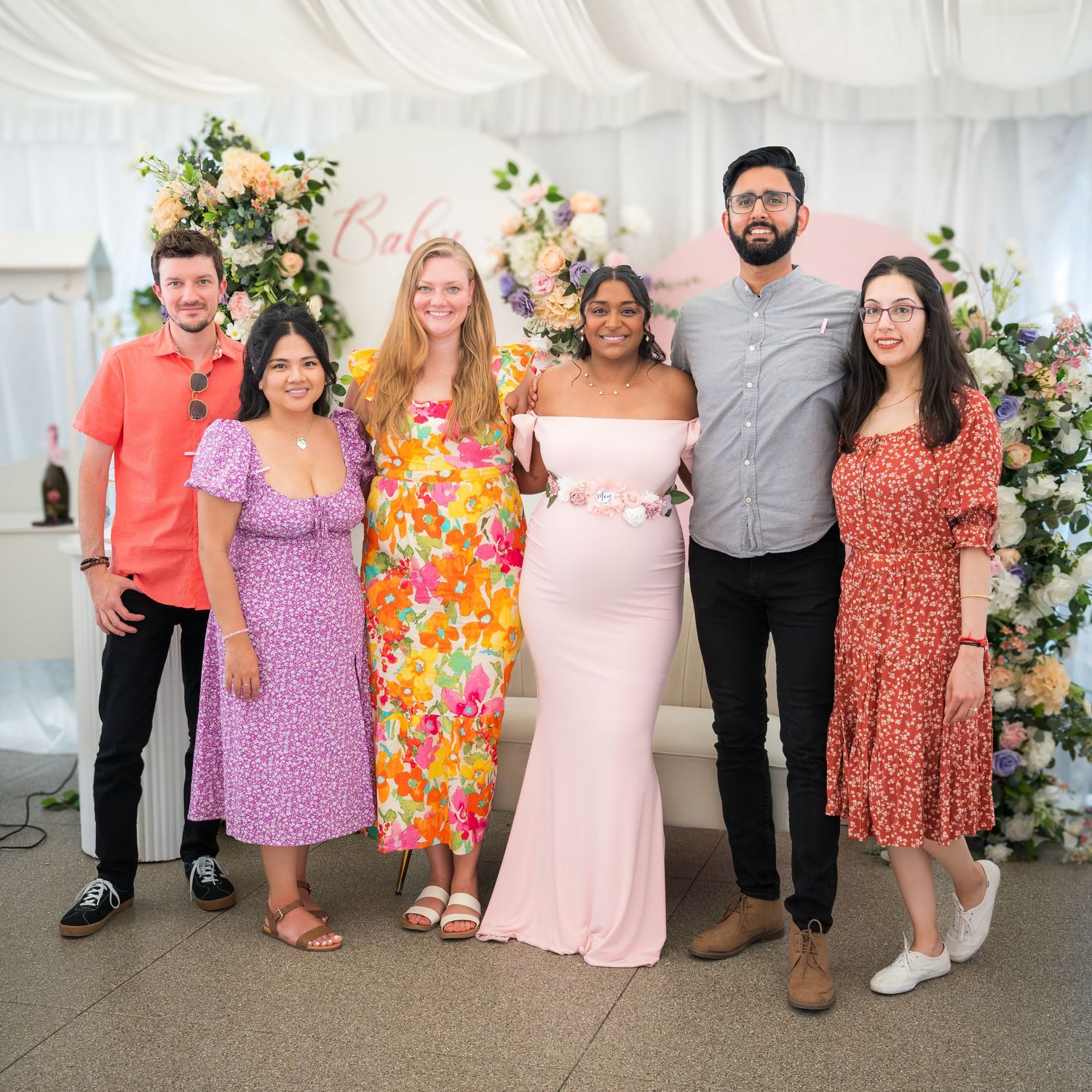Group standing together at a celebration with floral decorations and draped white fabric backdrop.