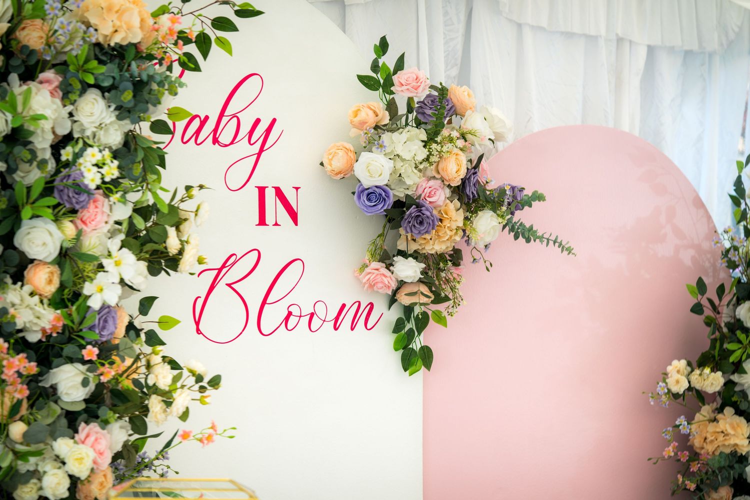 Pastel pink and white floral arrangements frame elegant cursive text at a baby shower celebration.