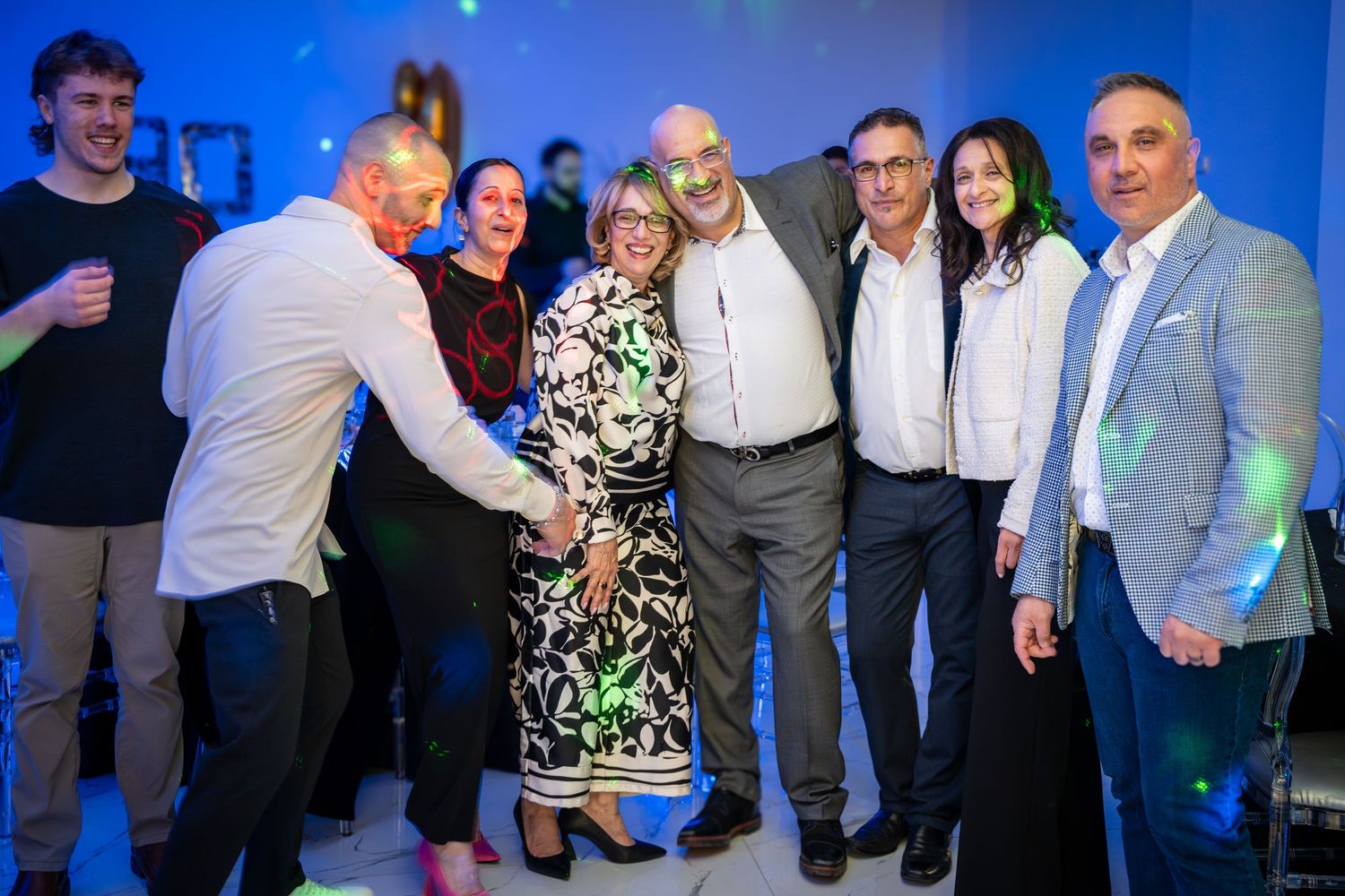 Group of party guests socializing and dancing at an indoor celebration with blue ambient lighting.