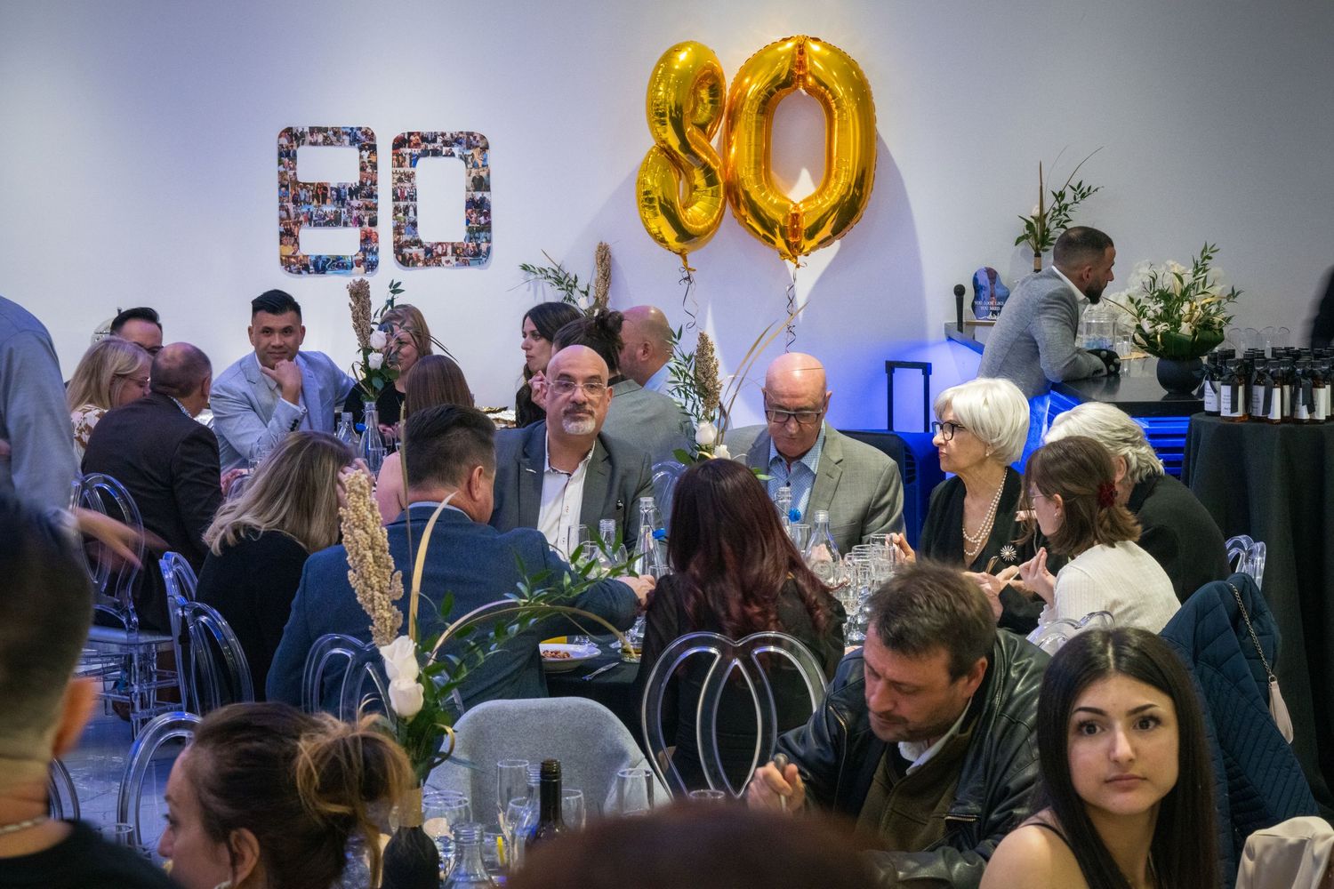 Party celebration with gold number 80 balloons and guests mingling in a decorated room.