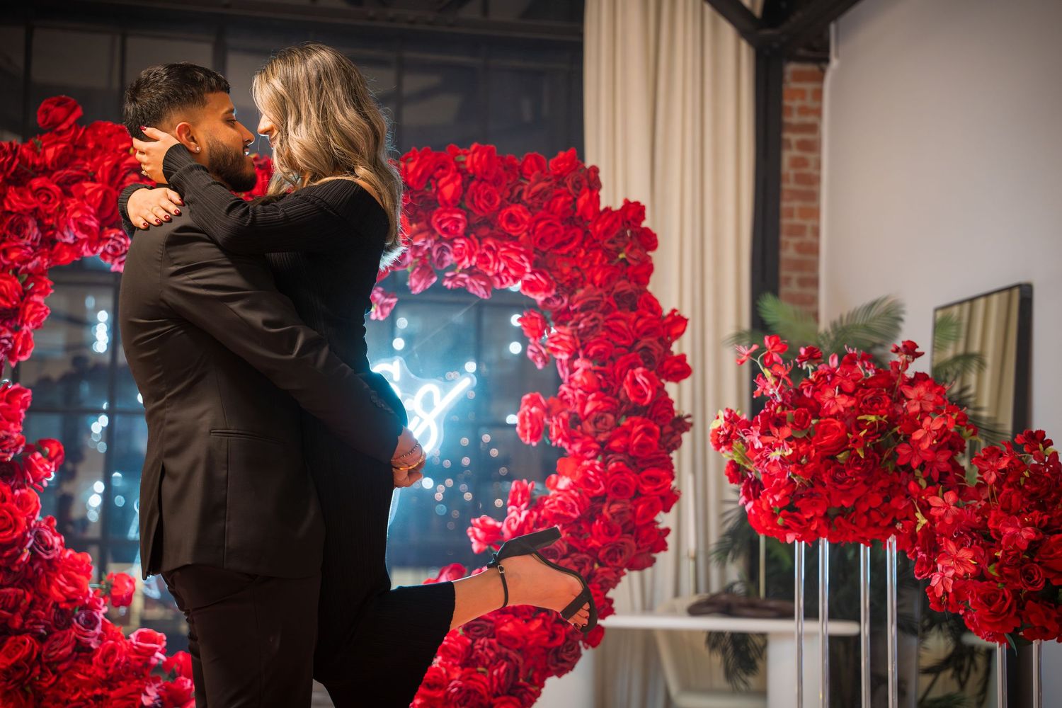 Romantic proposal setup with bright red roses and glowing lights in an indoor setting.