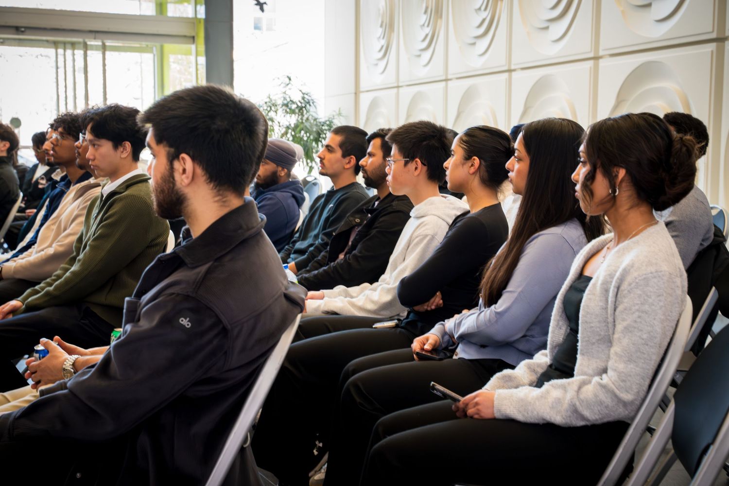Rows of conference attendees viewing a presentation in a modern meeting space with decorative wall panels.