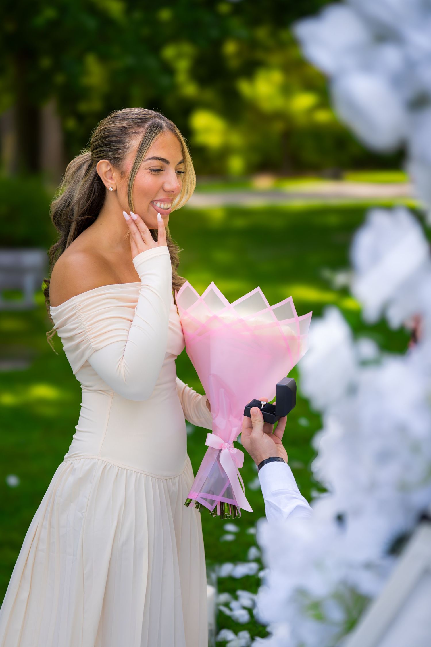 A couple shares an emotional moment during a surprise proposal surrounded by white floral decorations.