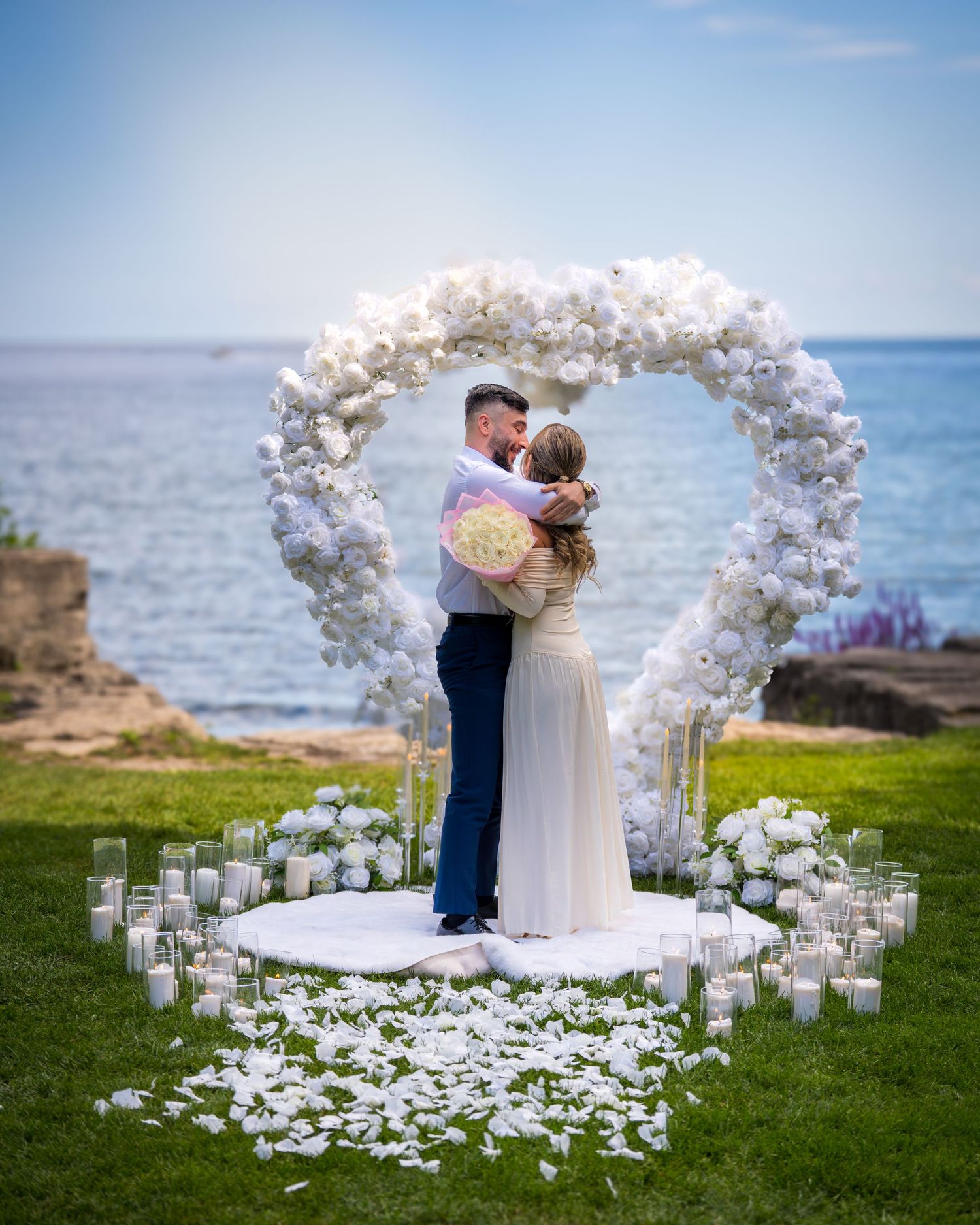 Elegant beachside wedding ceremony with white floral arch and candlelit aisle overlooking the ocean.