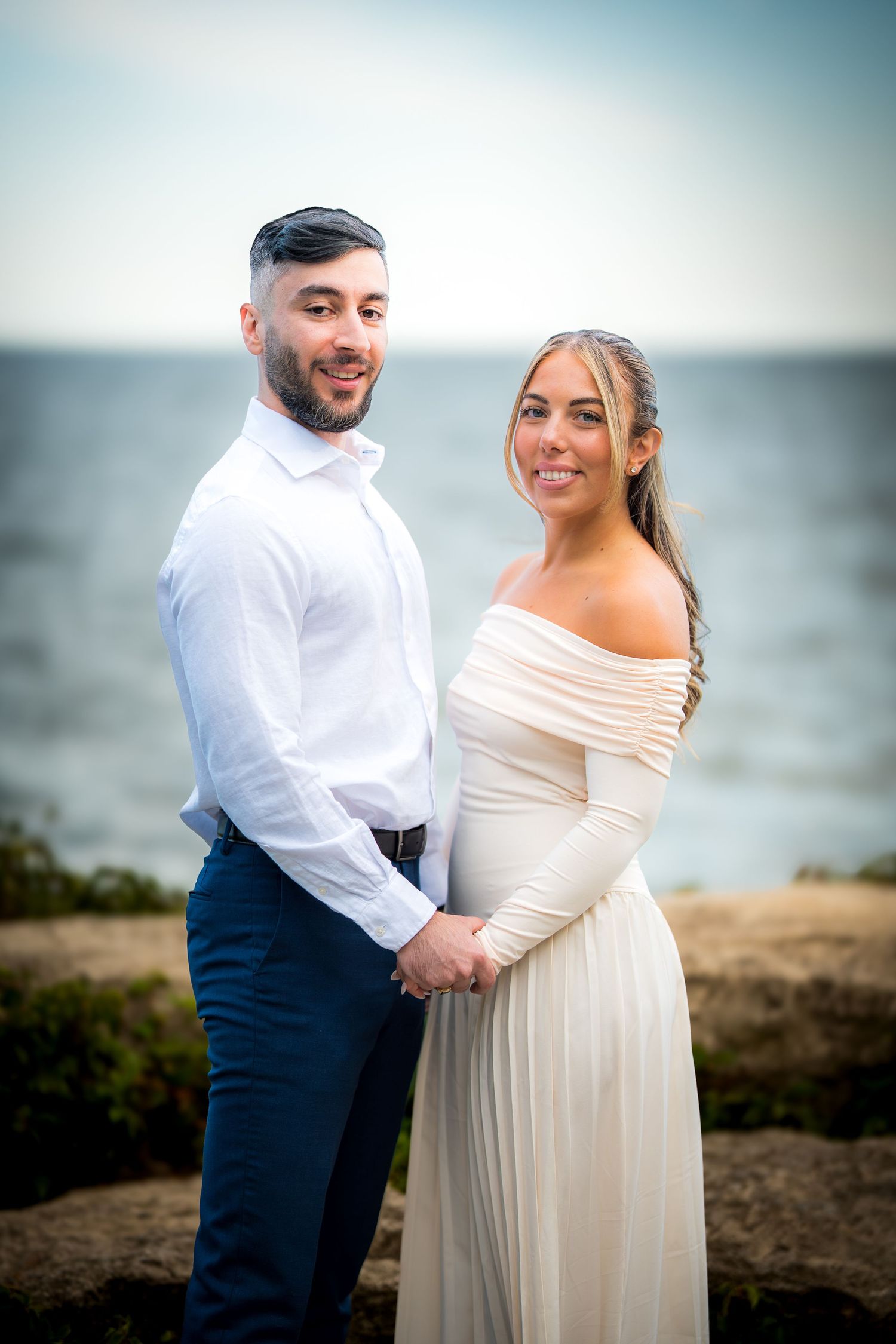Candid moments of a couple laughing and embracing on a coastal cliff during their wedding photoshoot.