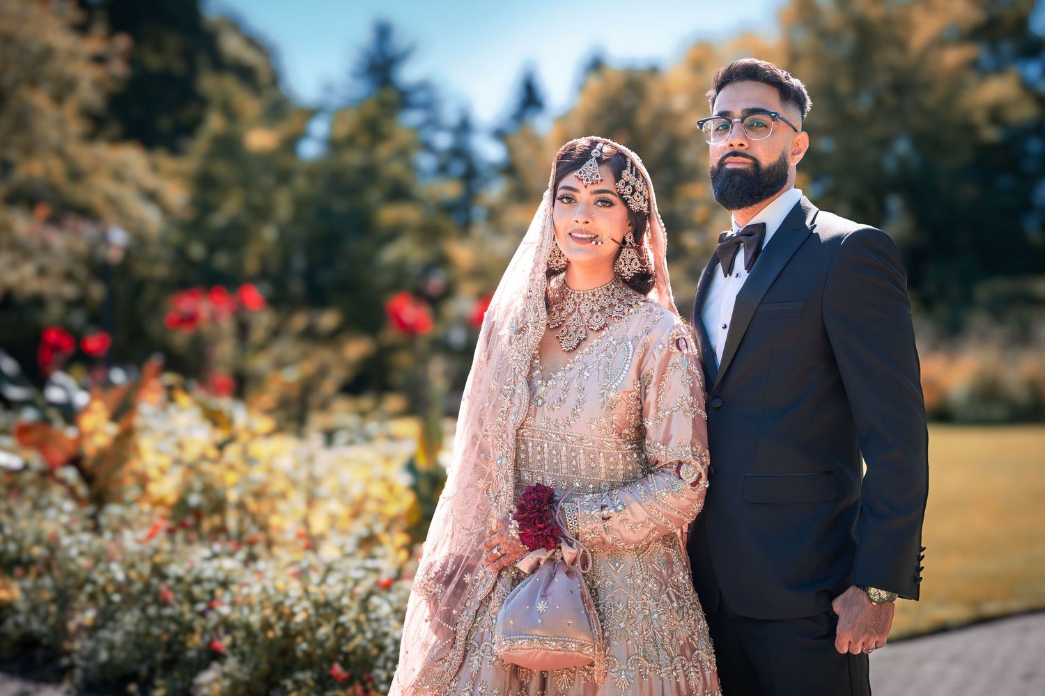 Traditional South Asian wedding couple poses in a garden setting with beautiful natural lighting and foliage.