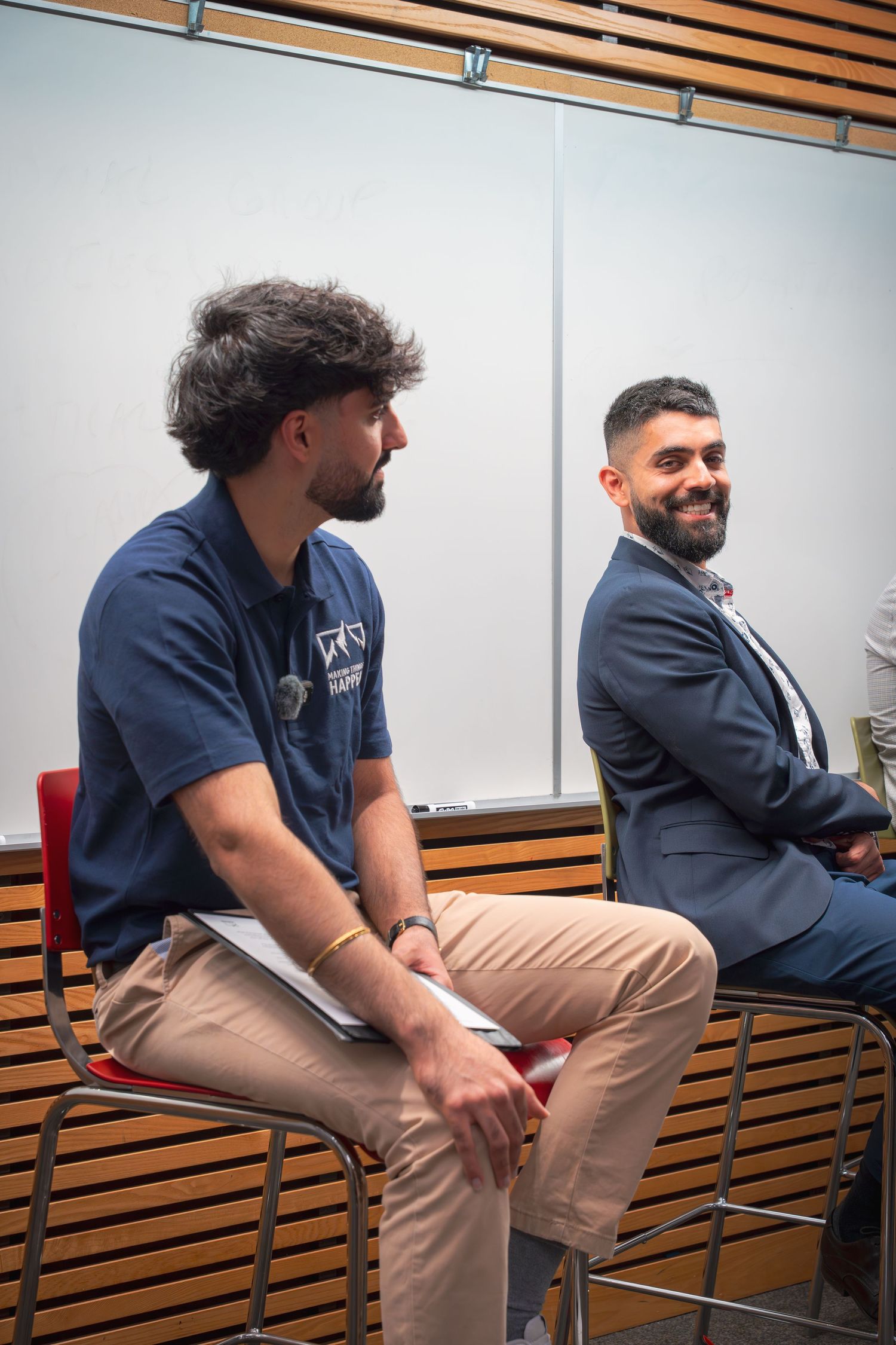 Two speakers sit on stools during a professional panel discussion in a modern conference room.