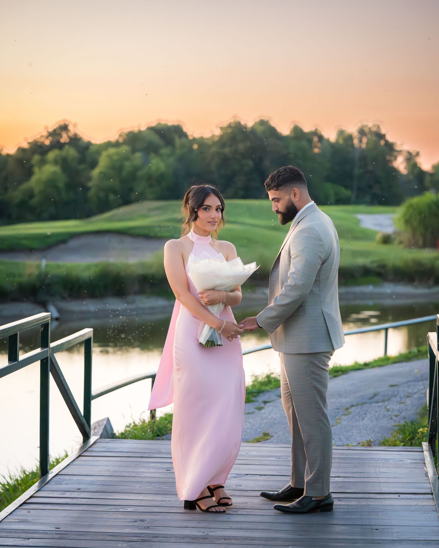 A couple shares an intimate moment on a lakeside boardwalk during sunset.