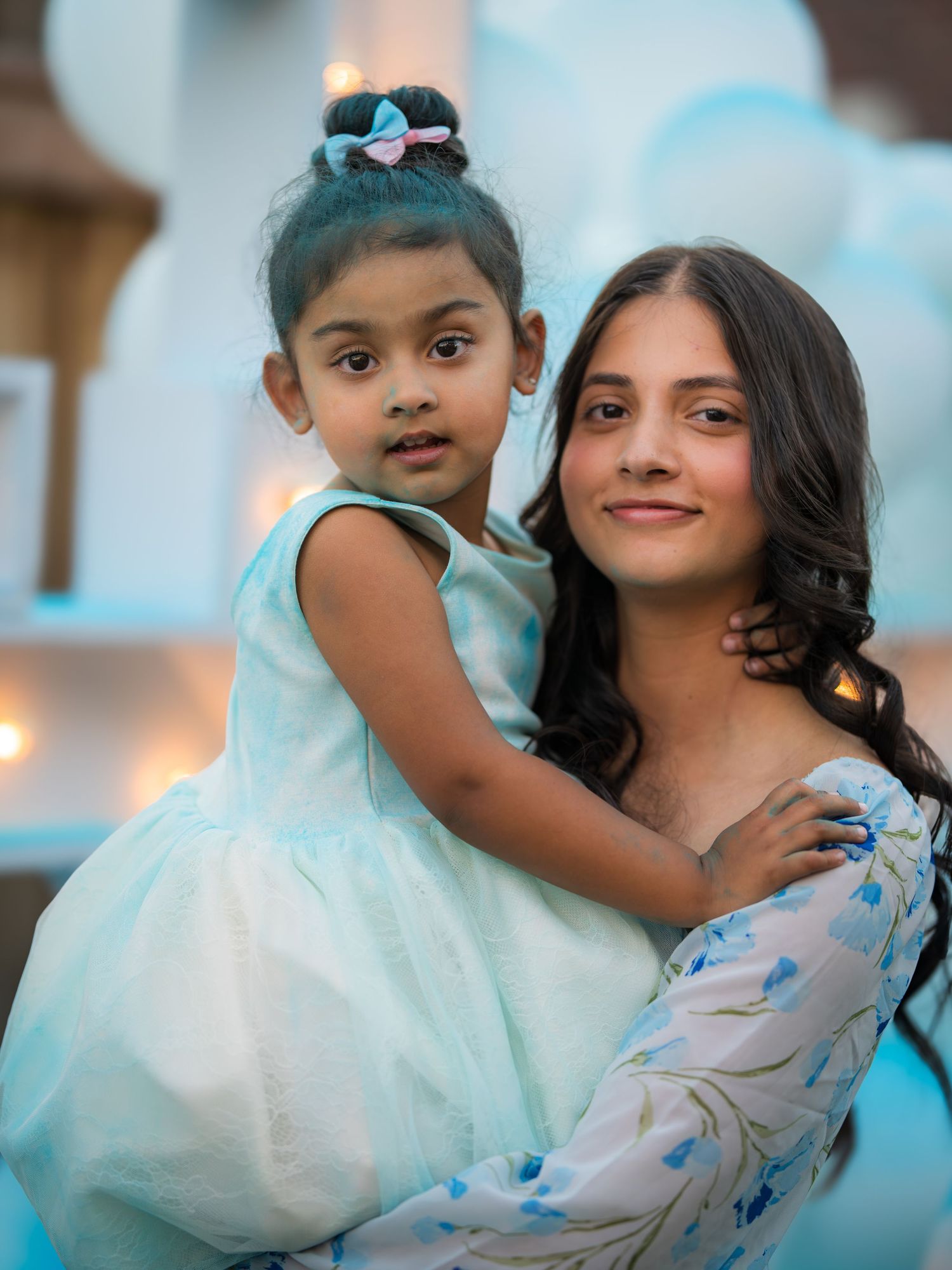 Woman in floral dress holding young girl in light blue dress at a baby shower event.