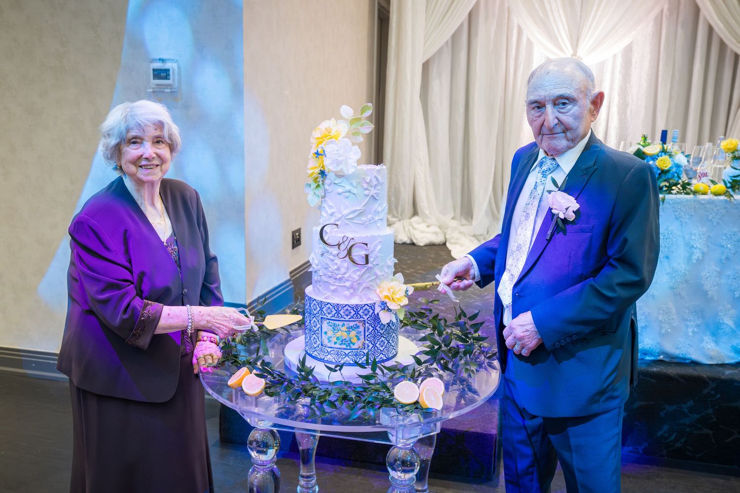 Elderly couple cutting their anniversary celebration cake decorated with monogram C and G at a formal reception.