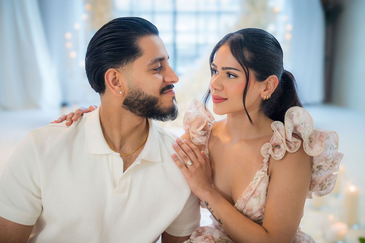 Couple gazing lovingly at each other seated together in a softly lit romantic indoor setting.
