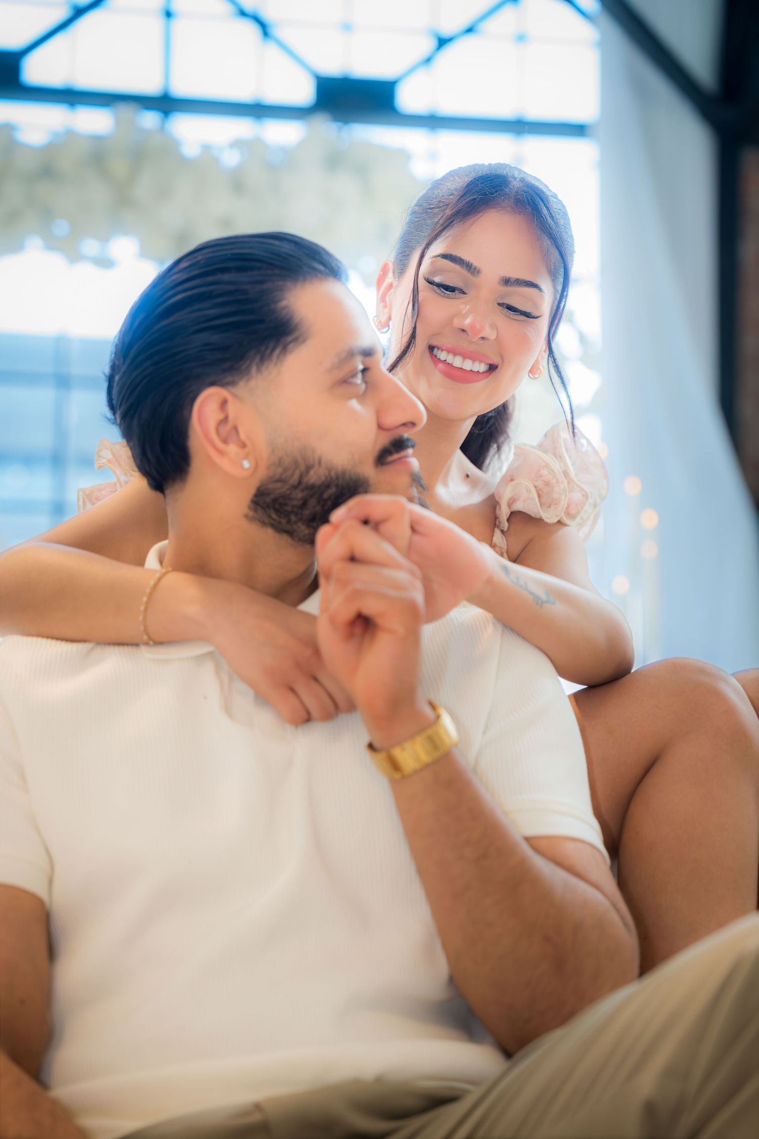 A couple sharing a tender moment, woman smiling while holding mans hand during a romantic indoor setting.