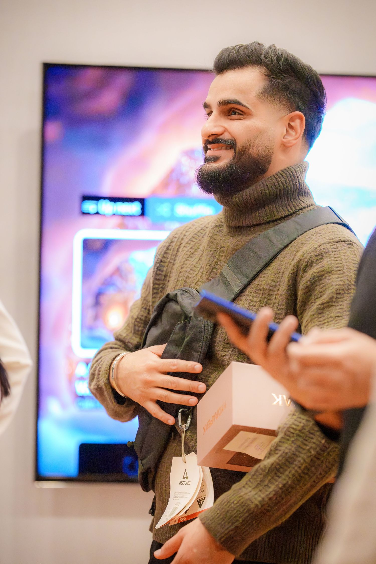 Person in brown turtleneck sweater laughing and gesturing during indoor gathering.
