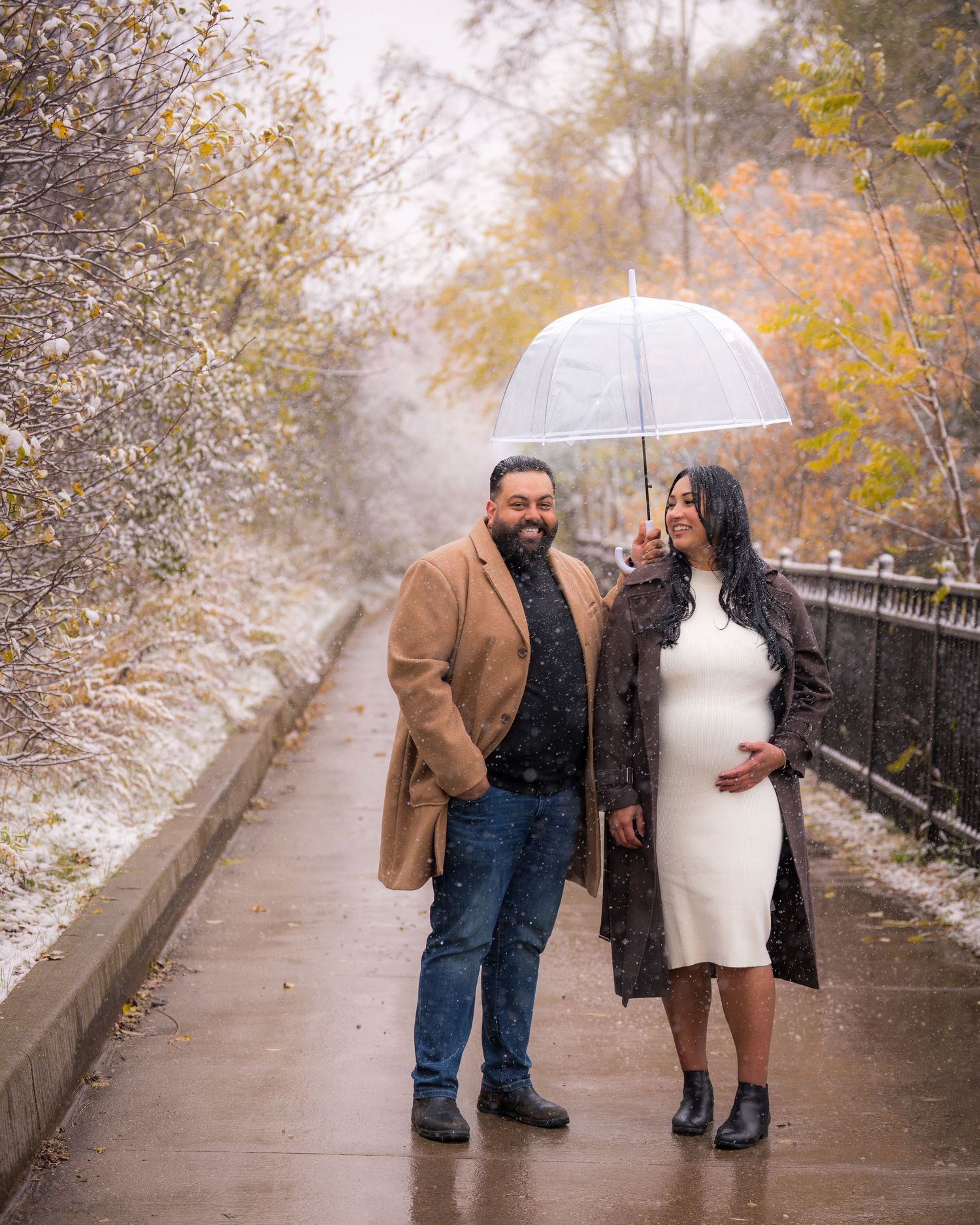 Couple walking together on snowy path under white umbrella in autumn setting.